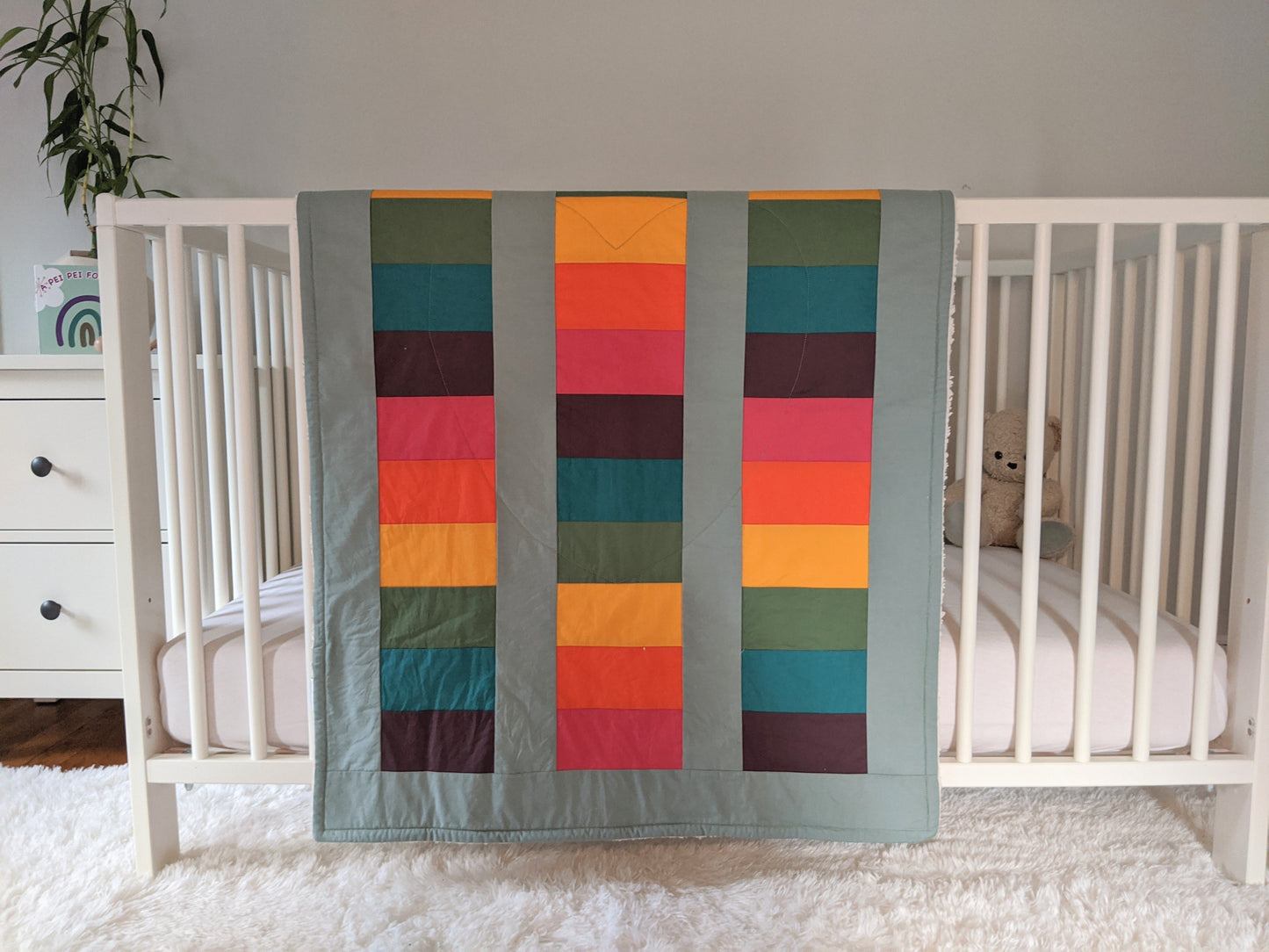 Bright Rainbow on Sage, backed with Fluffy Sherpa, Original, hangs over the side of a crib in a nursery